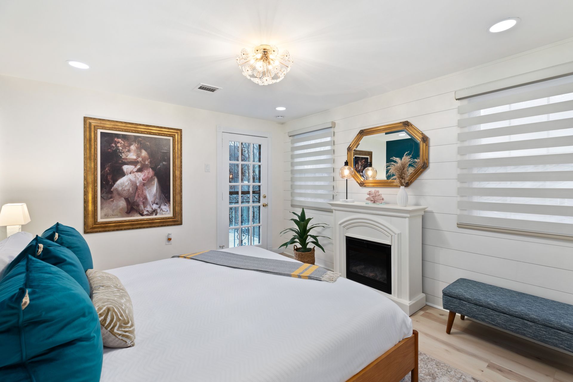 A bedroom with a bed , fireplace , mirror and bench.