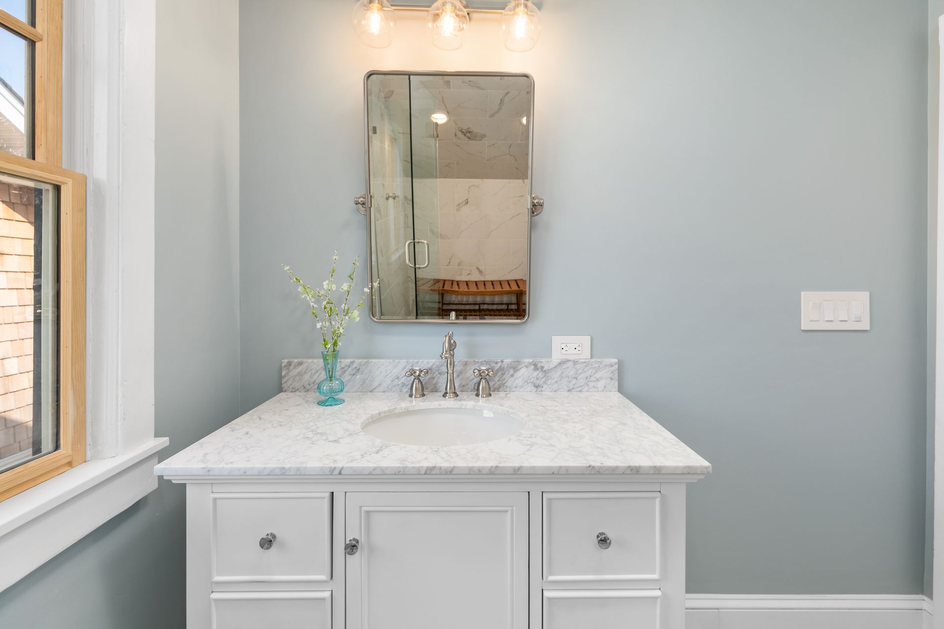 A bathroom with a sink , mirror and window.