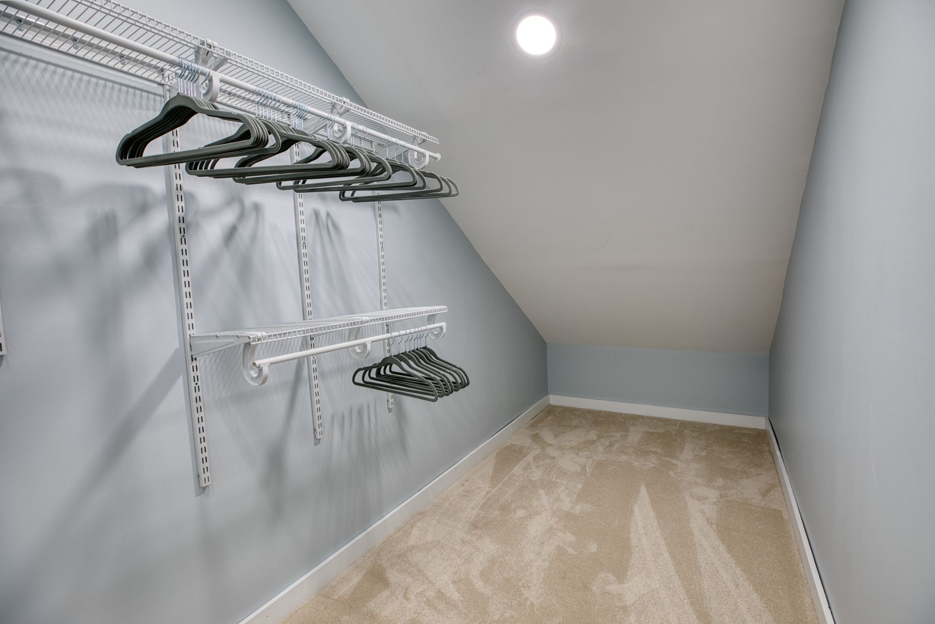 A walk in closet with a slanted ceiling and a lot of clothes hanging on the racks.