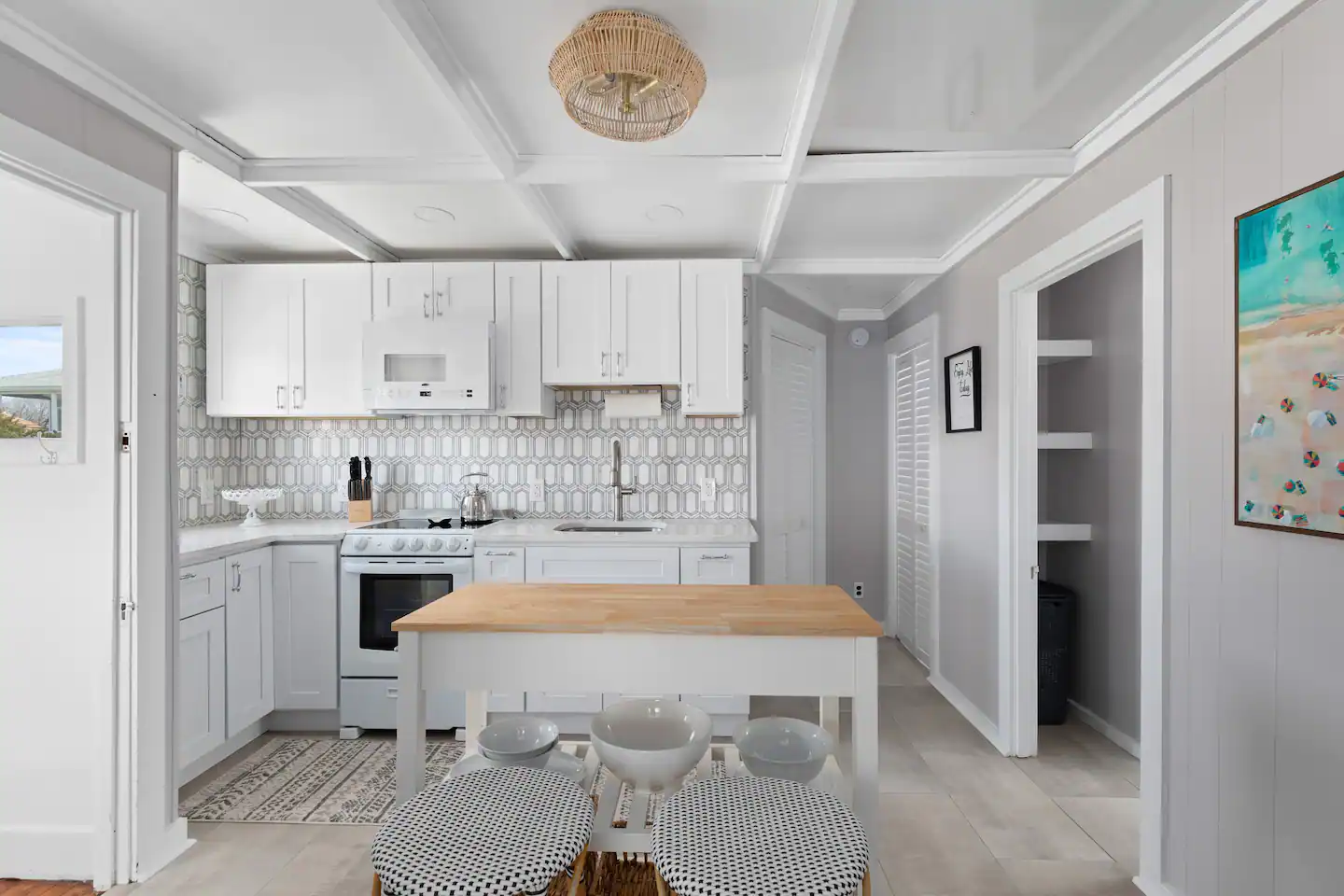 A kitchen with white cabinets , a stove , a table and a painting on the wall.