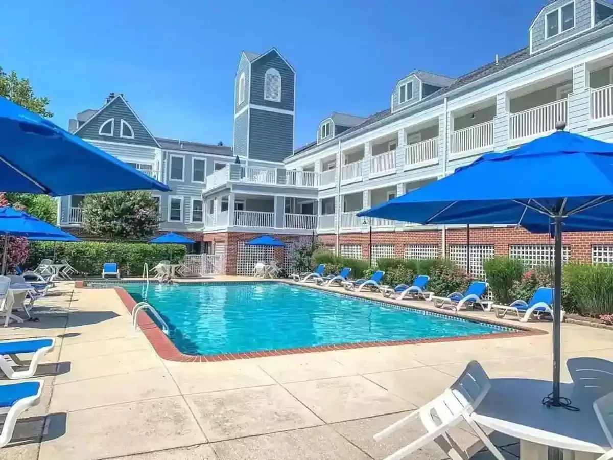 A large swimming pool surrounded by chairs and umbrellas in front of a hotel.