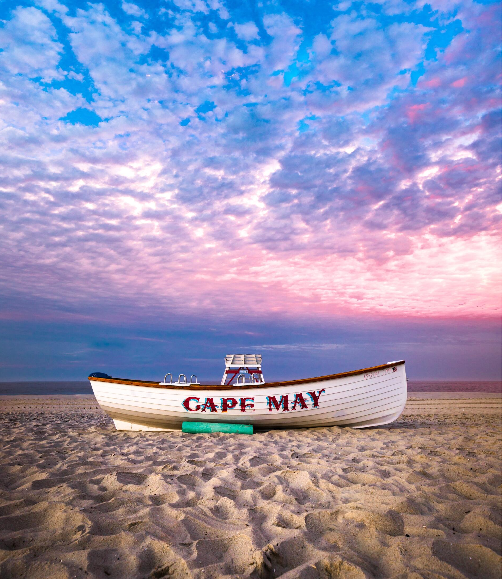 A boat called cape may is on the beach at sunset.