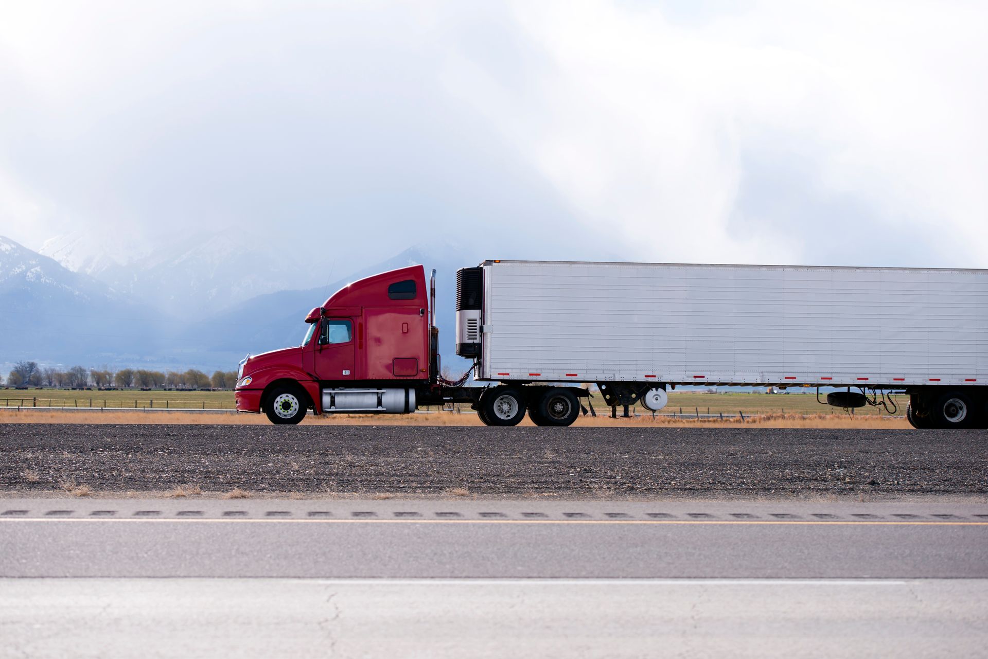 A red semi truck with a white trailer is driving down a highway.