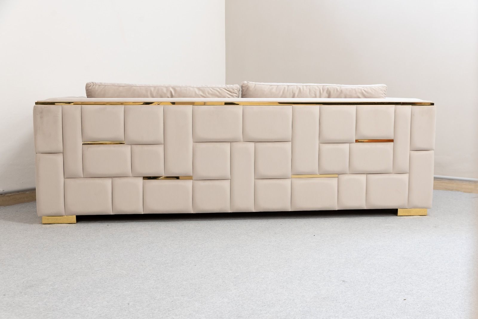 Divano beige con dettagli dorati in una stanza con pareti e pavimenti chiari.