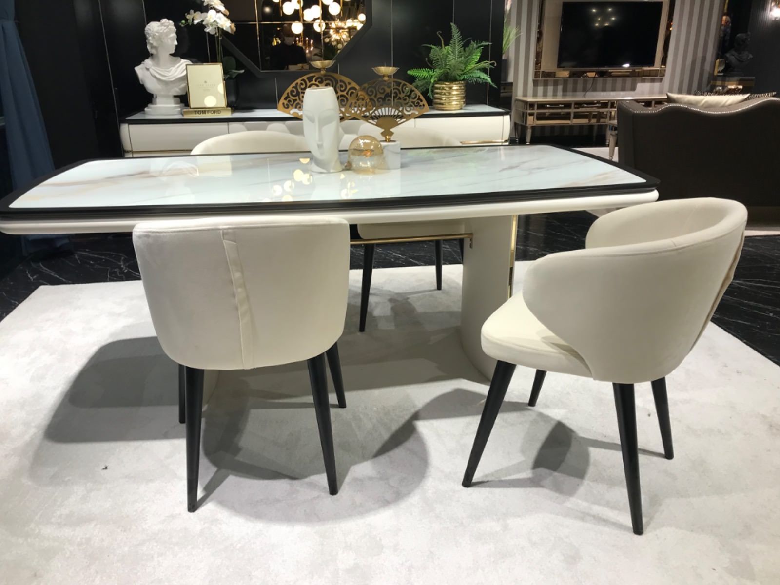 Set da pranzo con tavolo effetto marmo, sedie color crema, gambe nere e dettagli decorativi.