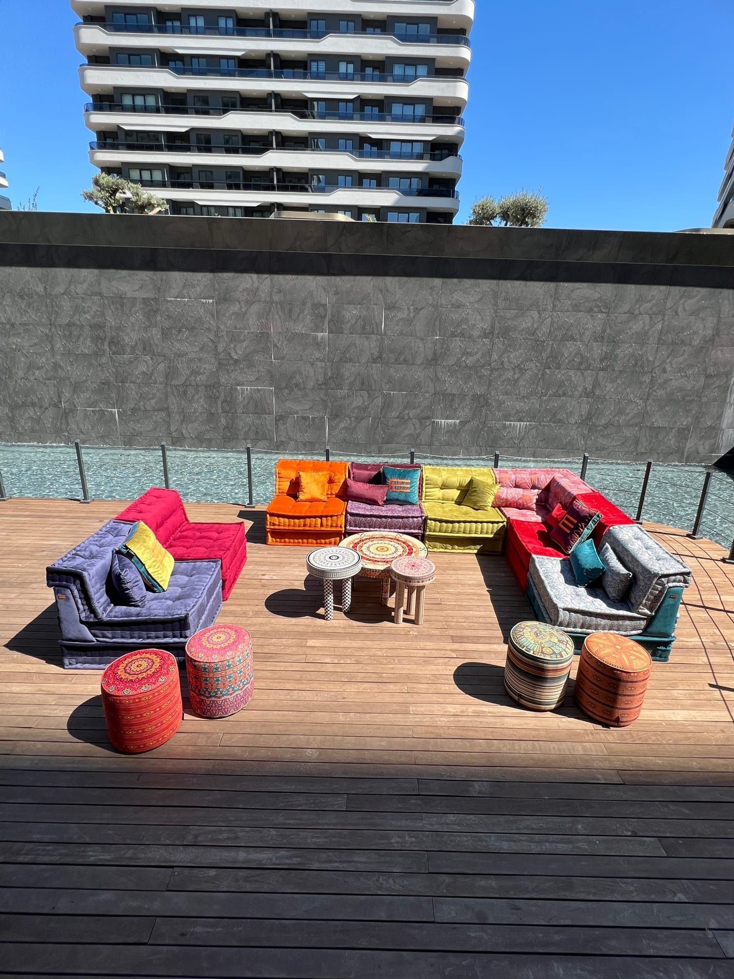 Mobili da esterno colorati su una terrazza in legno con un edificio sullo sfondo.
