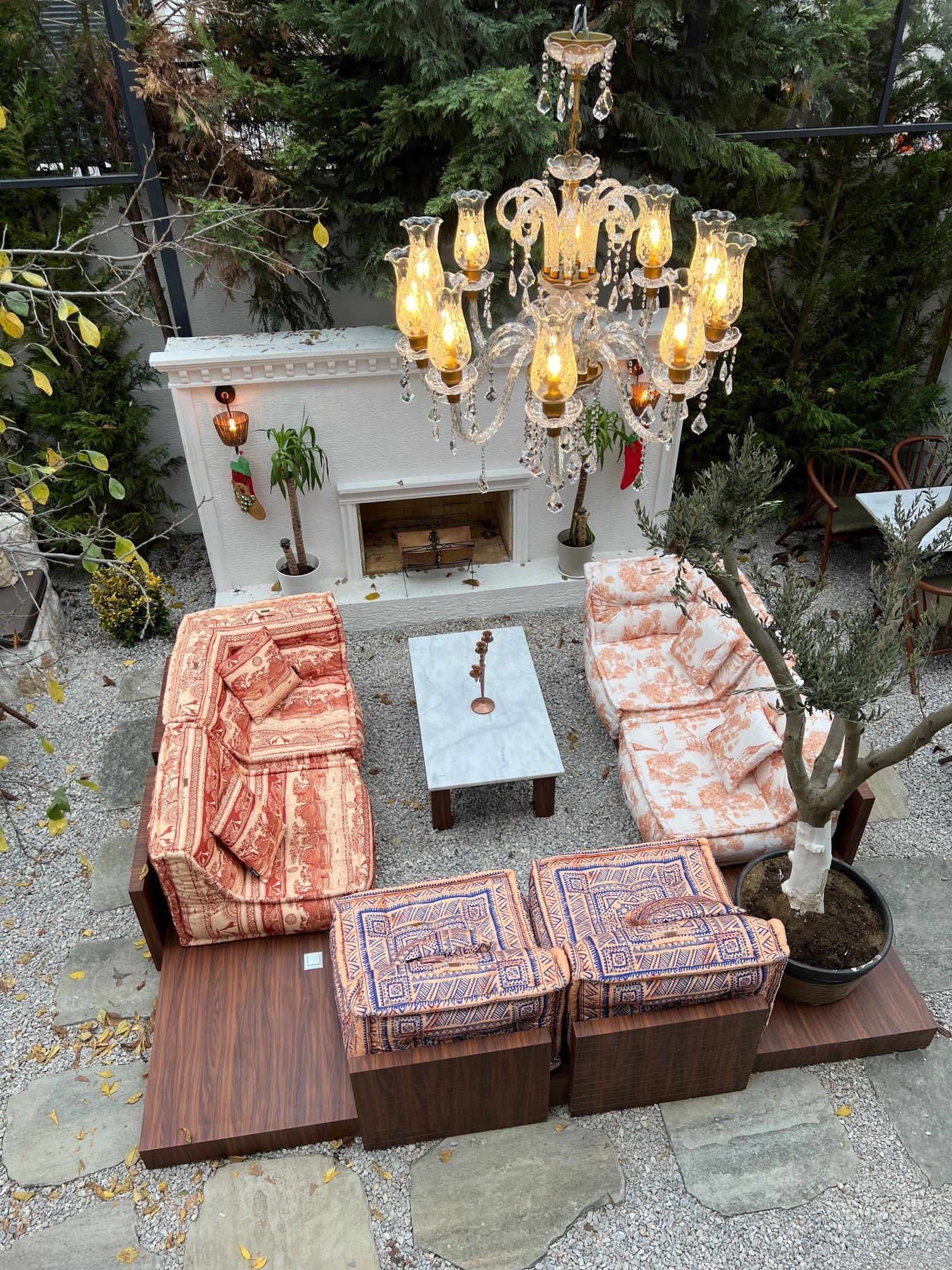 Area salotto all'aperto con camino, lampadario e mobili decorati su un patio in pietra.