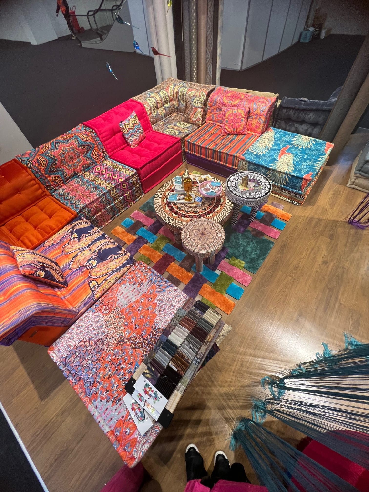 Divano componibile con motivi colorati, tappeto, tavoli e campioni di tessuto in uno showroom.