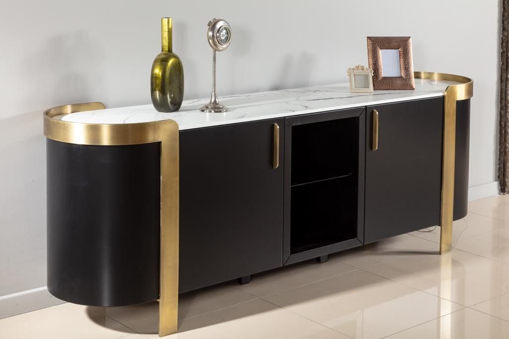 Mobiletto nero e oro con piano in marmo, che espone oggetti decorativi in un ambiente neutro.