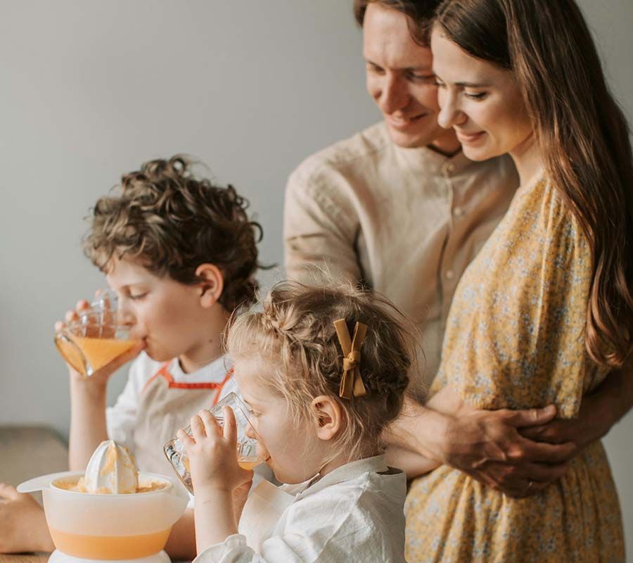 Family of four sharing breakfast, with children drinking orange juice at a table