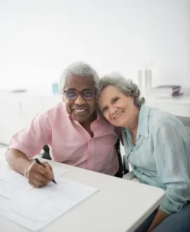 Dental staff in gray uniforms work in a bright clinic, one at a computer and one near the wall.