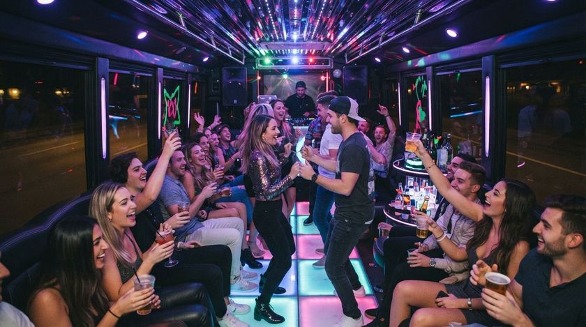 People dancing and cheering in a neon-lit party bus with drinks raised and colorful lights overhead