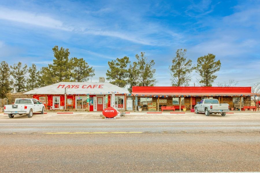 Small roadside cafe with a red awning, parked cars, and a wide empty street under a blue sky.