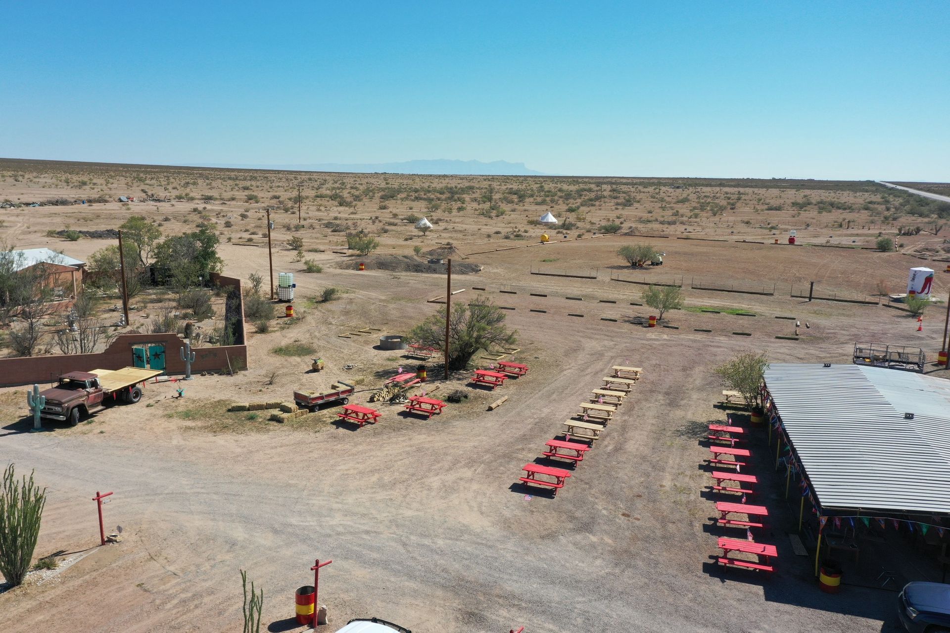 Desert campsite with rows of red vehicles beside tents and a striped roof under a clear blue sky