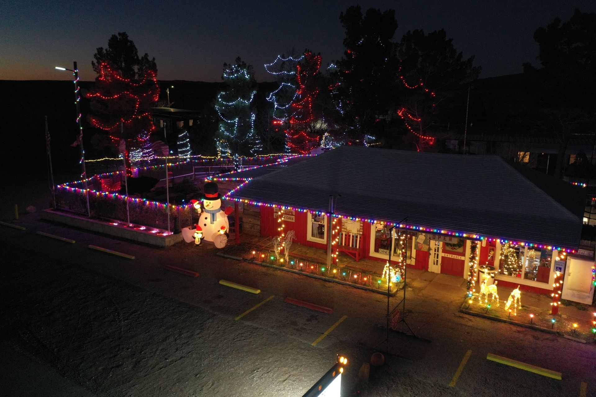 House lit with colorful holiday lights at night, with a snowman decoration in front.