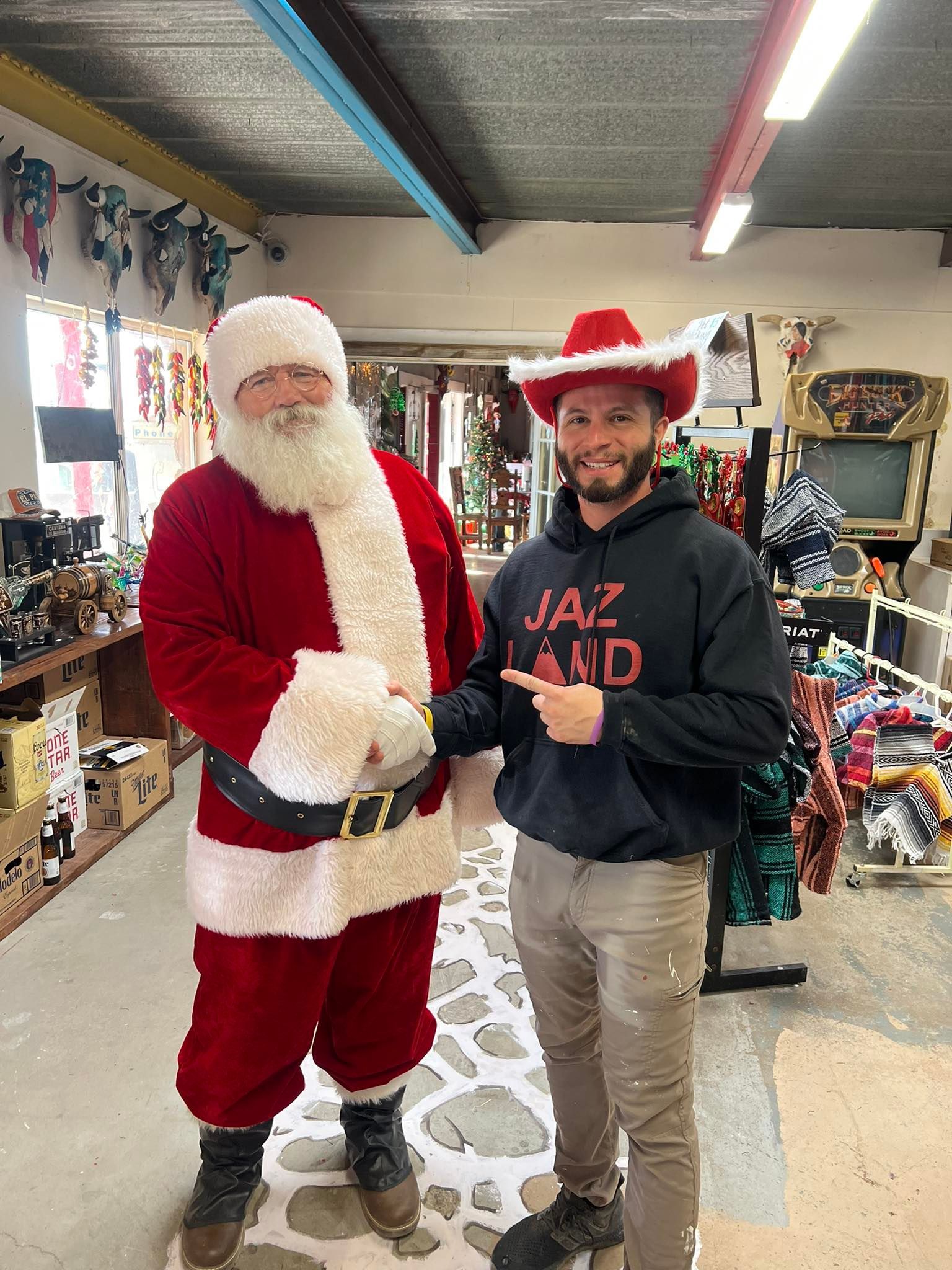 Santa beside a smiling person in a red cowboy hat inside a festive store