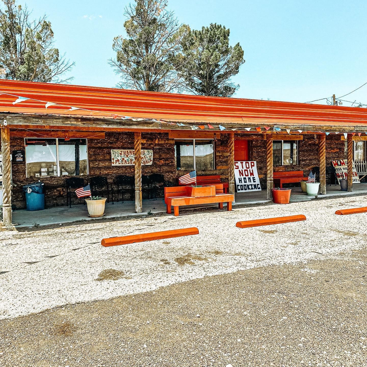 Rustic roadside store with orange awning, benches, and signs under a bright blue sky
