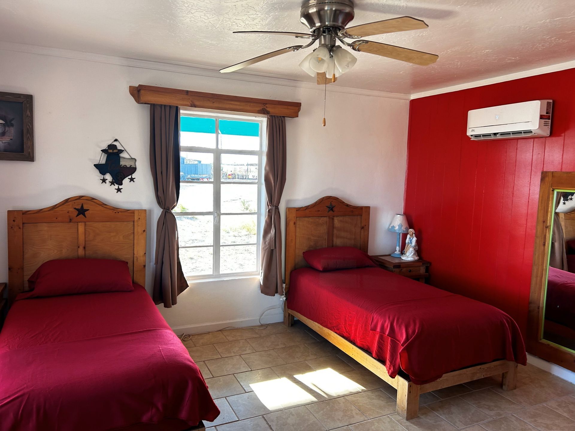 Bedroom with two twin beds, red bedspreads, white walls, a window, and a ceiling fan.