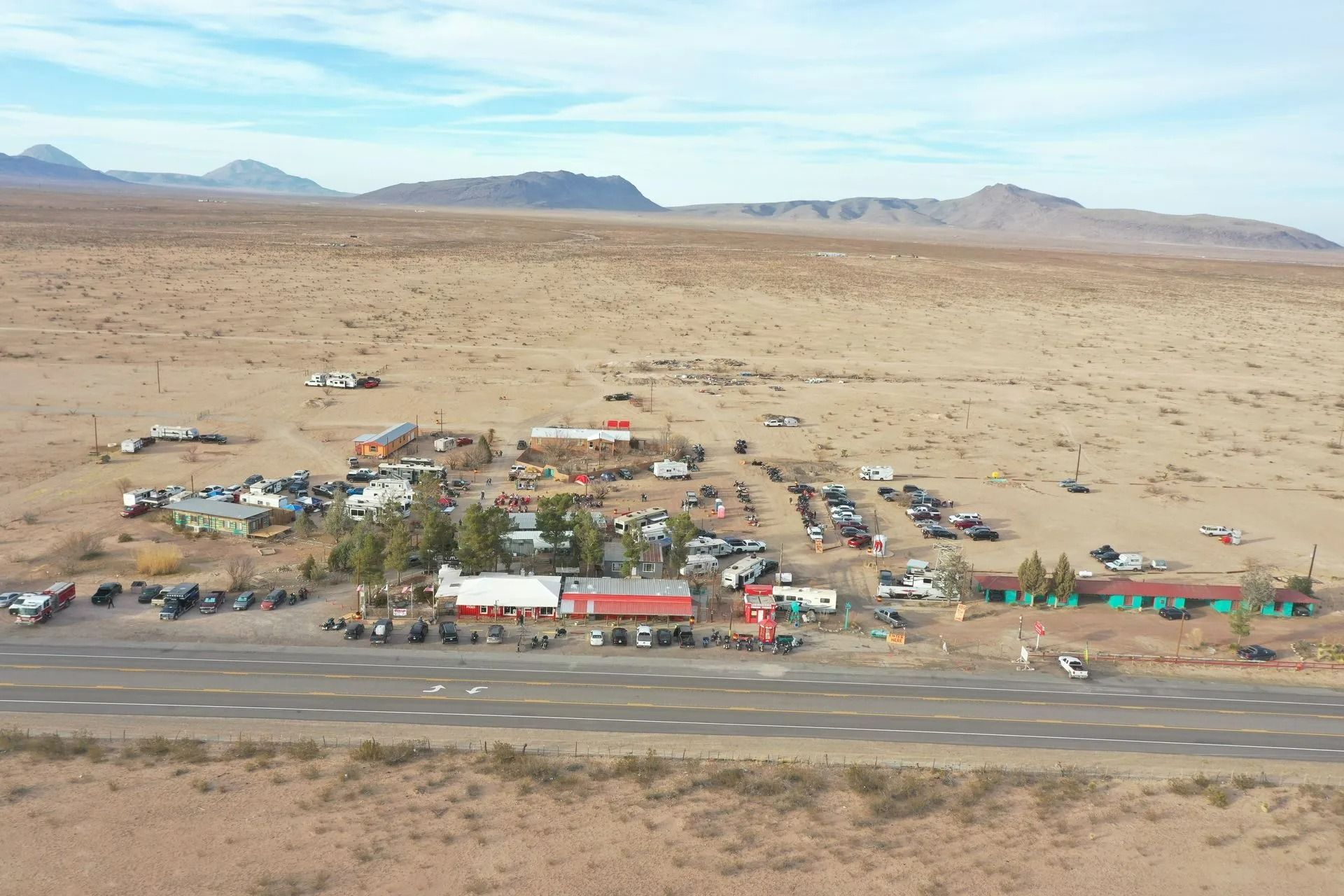 Small desert settlement beside a road, with scattered buildings and mountains in the distance
