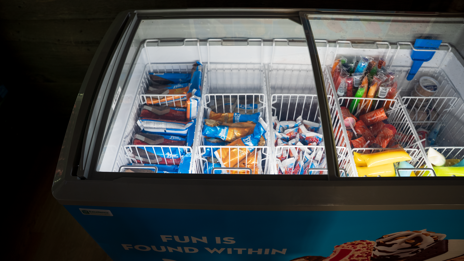 Open-top freezer display with assorted colorful ice cream bars and treats in wire baskets