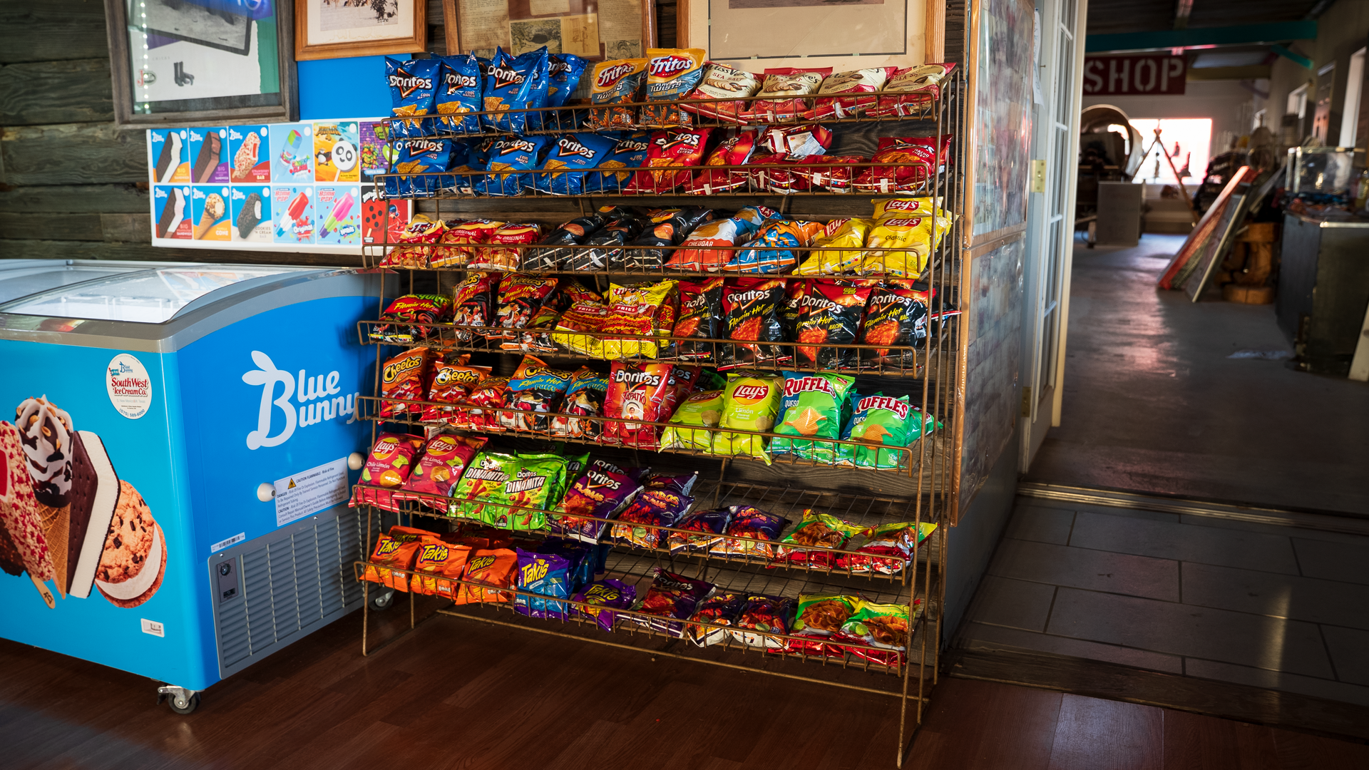 Snack rack beside a blue ice cream freezer in a small shop aisle