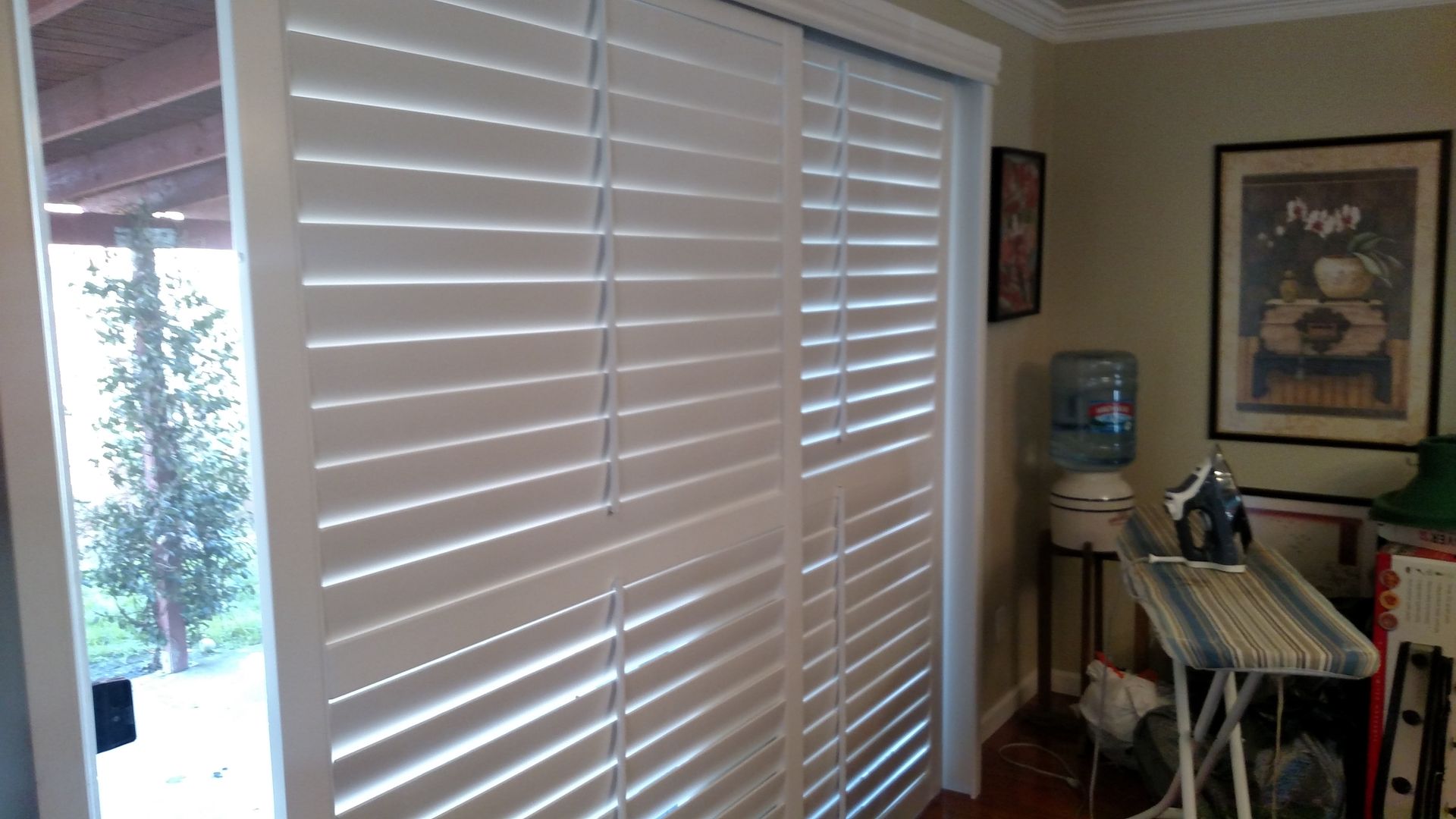 A room with a sliding glass door and white shutters on it.