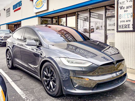 A tinting installation on a tesla model x is parked in a parking lot in front of a building.