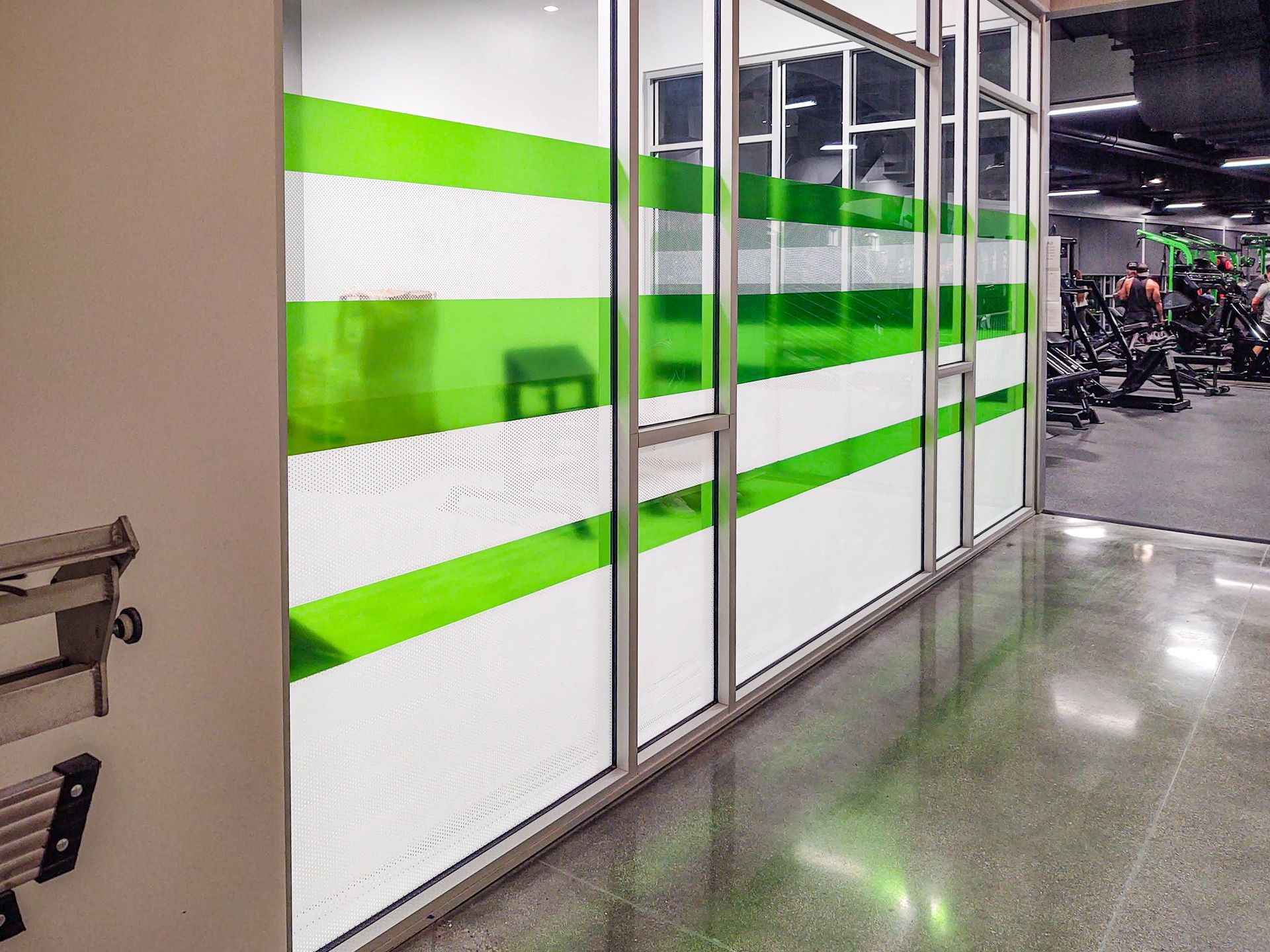 A hallway in a gym with green and white stripes on the windows.