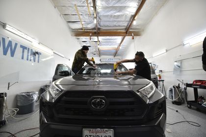 Two men are Appling automotive window tint on a toyota rav4 in a garage.