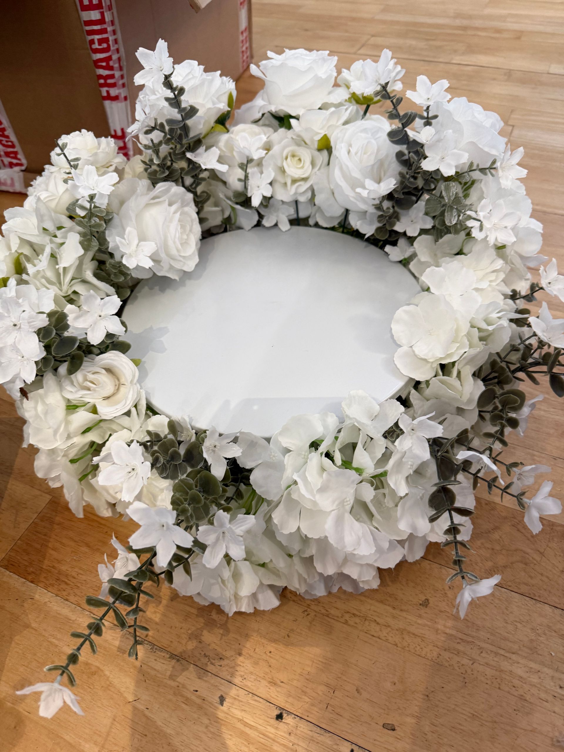 White floral funeral wreath with a blank center, laid on a wooden floor.