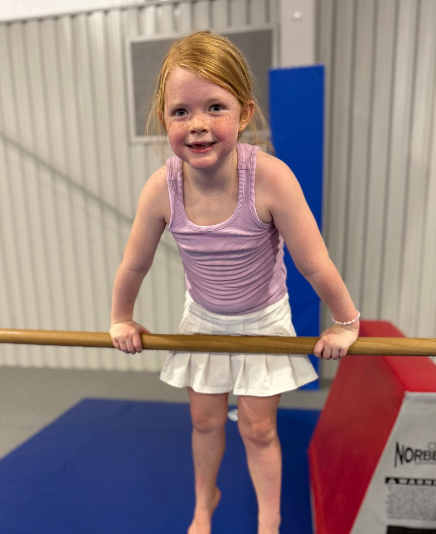 A young girl is standing on a pink mat in a gym.