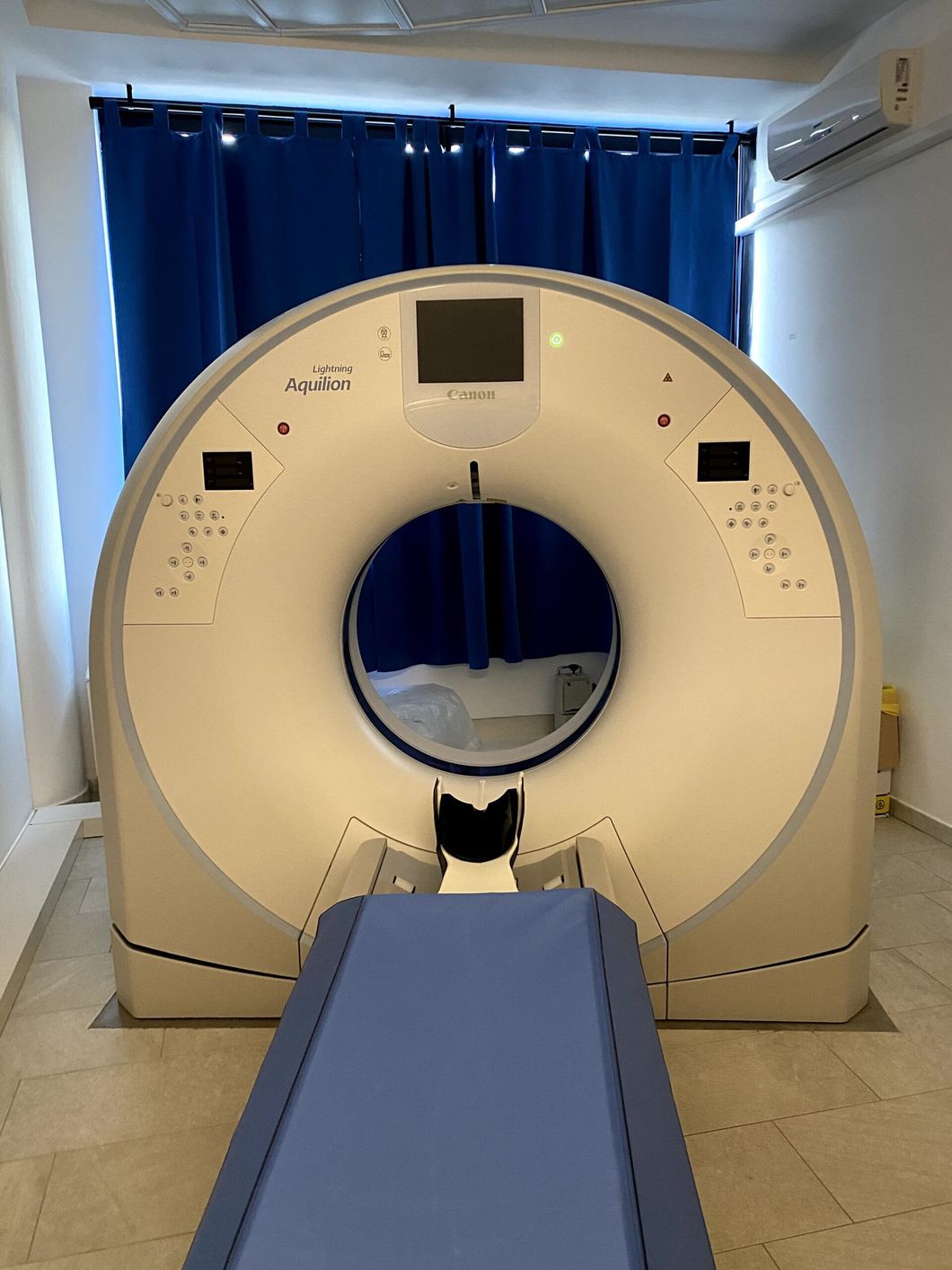 TAC in una stanza medica con un lettino per il paziente e tende blu sullo sfondo.