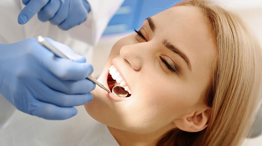 Un dentista esamina la bocca aperta di un paziente sorridente con uno specchietto dentale e le mani guantate.