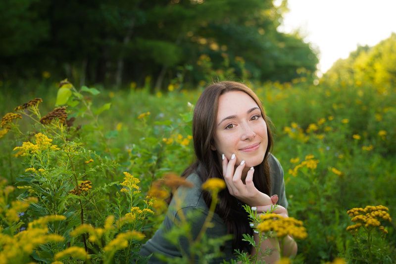 A young woman is sitting in a field of yellow flowers.