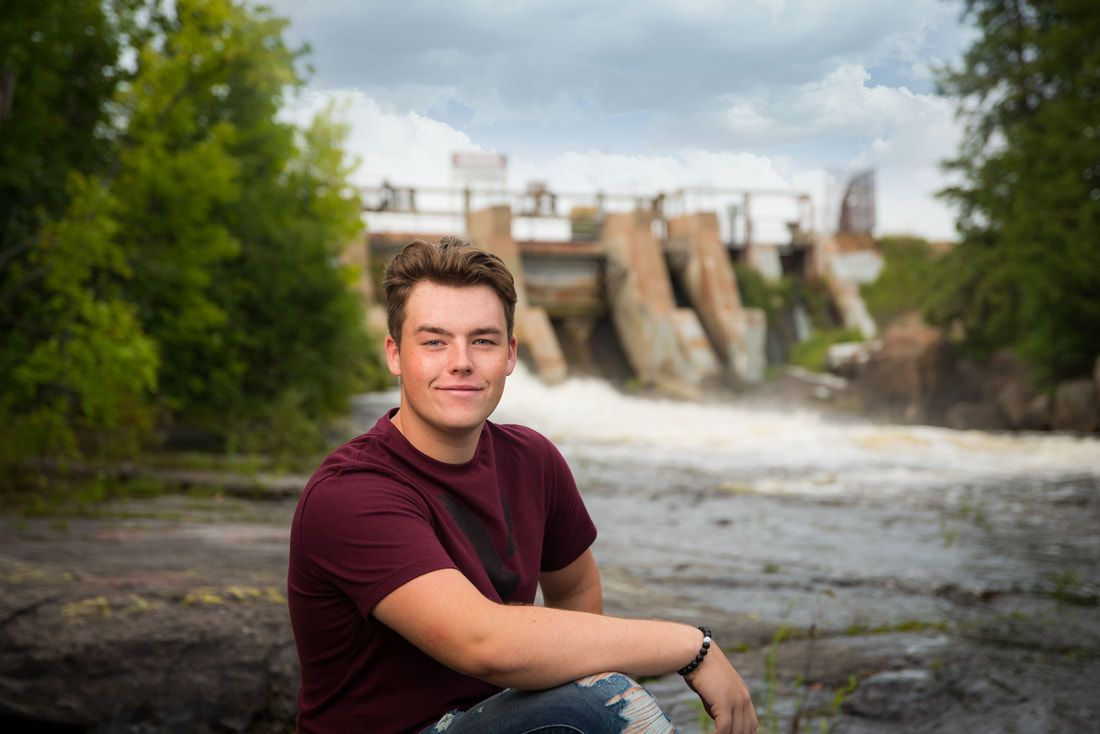 A young man is sitting on a rock in front of a waterfall.