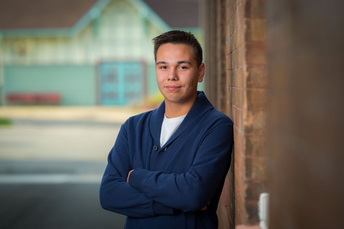 A young man is leaning against a wooden wall with his arms crossed.