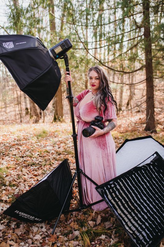 A woman in a pink dress is standing in the woods holding a camera.