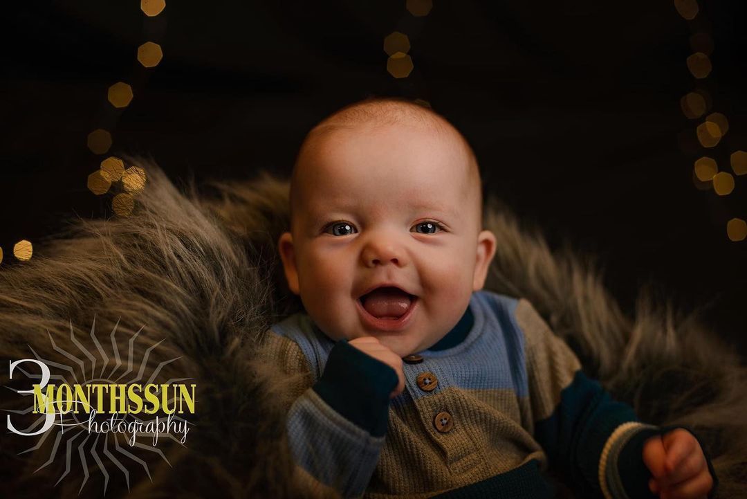 A baby is laying on a furry blanket and smiling.