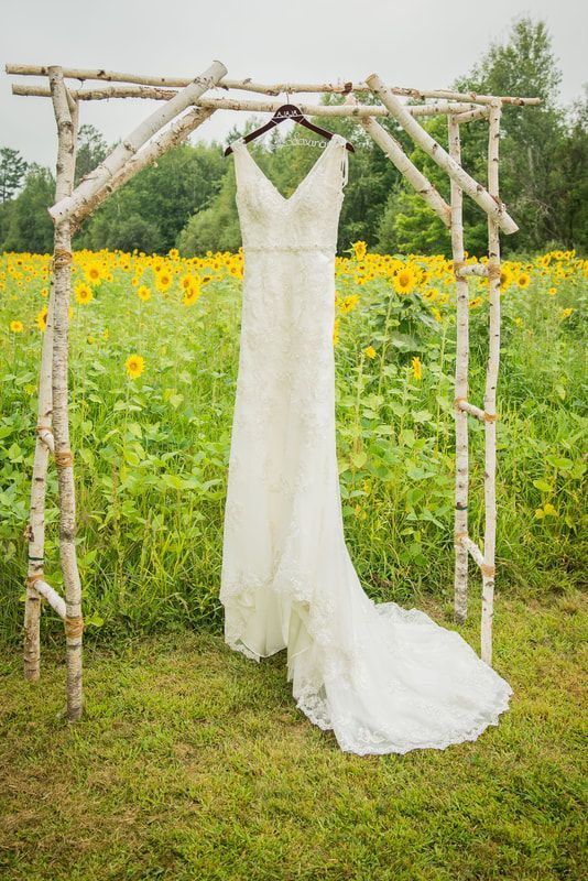 A wedding dress is hanging on a wooden arch in front of a field of sunflowers.
