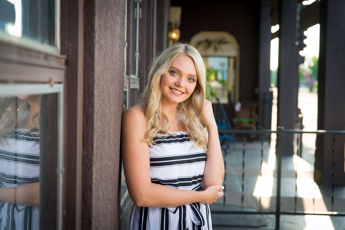 A woman in a striped dress is leaning against a wall and smiling.