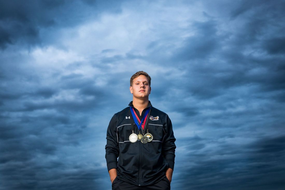 A man wearing a medal around his neck is standing in front of a cloudy sky.