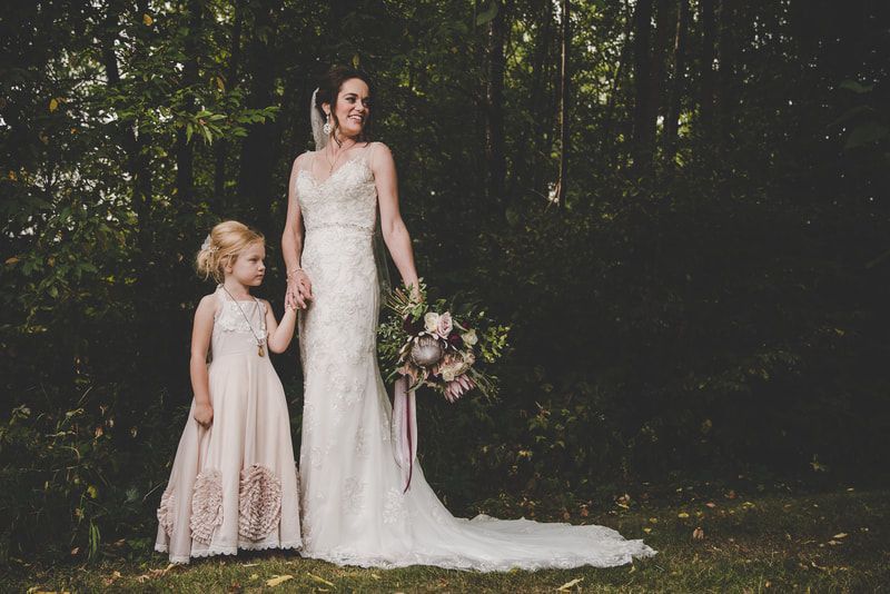 A bride and her flower girl are posing for a picture in the woods.