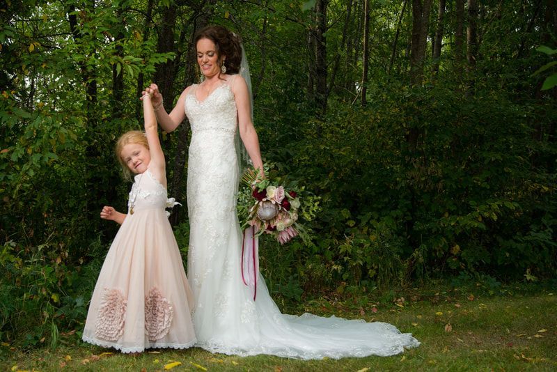 A bride and her flower girl are posing for a picture in the woods.