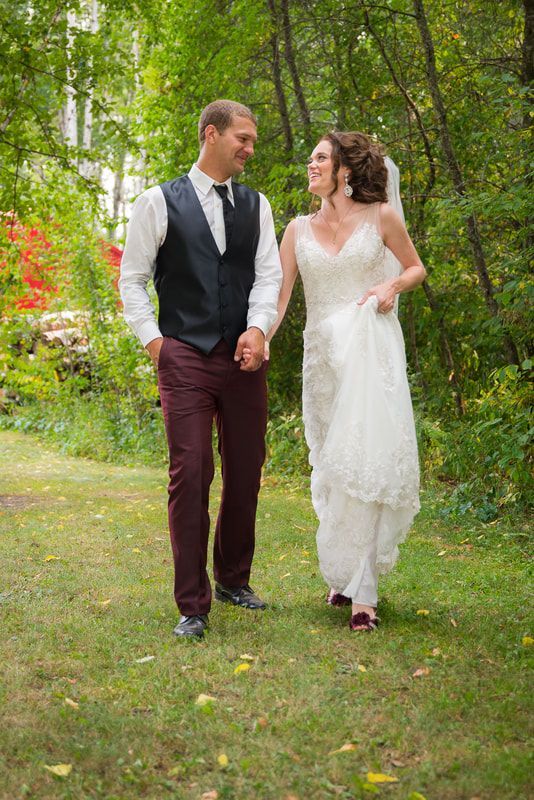 A bride and groom are walking in the grass holding hands.