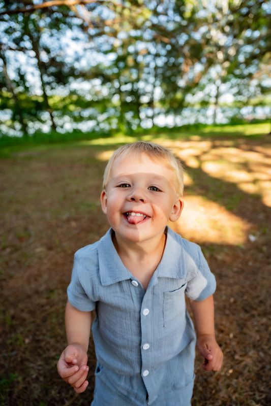A little boy is sticking his tongue out while standing in a park.