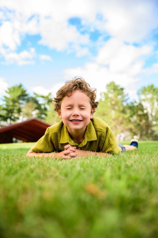 A young boy is laying on his stomach in the grass.
