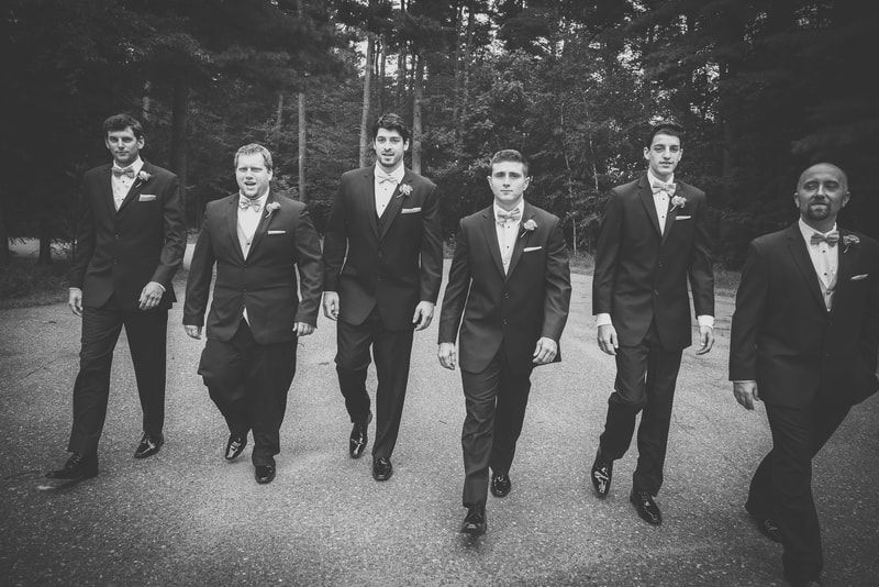 A group of men in suits and bow ties are walking down a road.