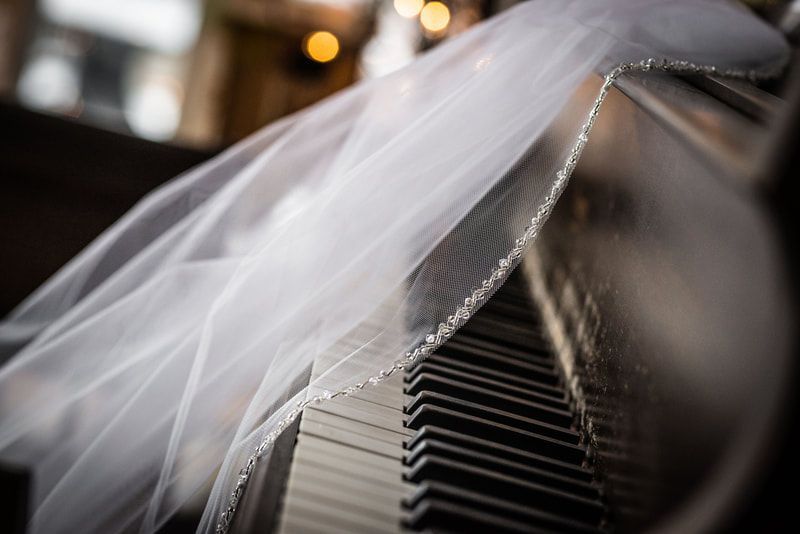 A bride wearing a veil is sitting on a piano.