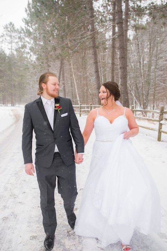 A bride and groom are walking in the snow holding hands.