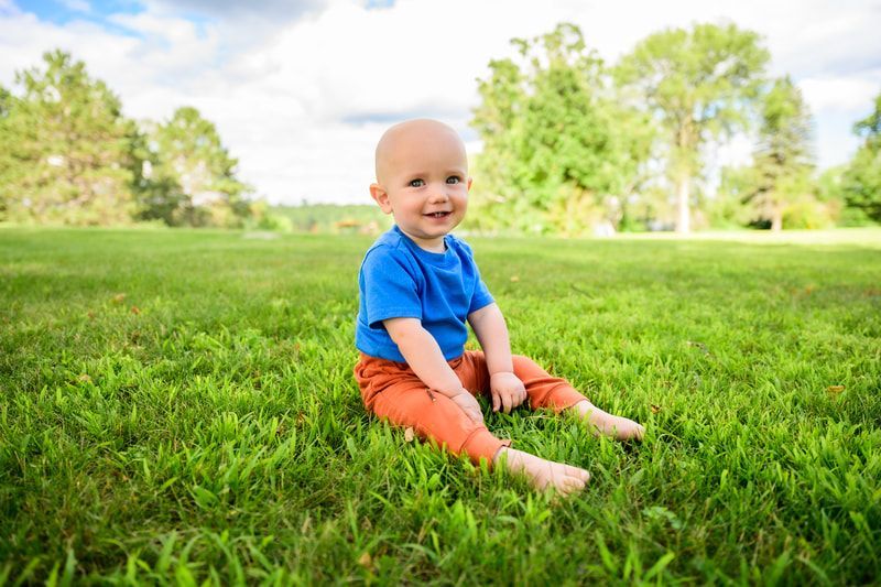 A baby is sitting on the grass in a park.